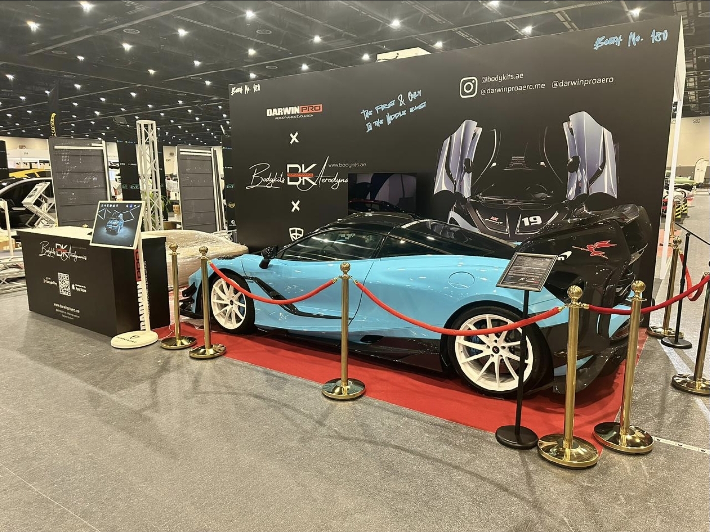 The DarwinPRO × BK Aerodynamics booth featuring the McLaren GTR build on a red carpet with gold stanchions.