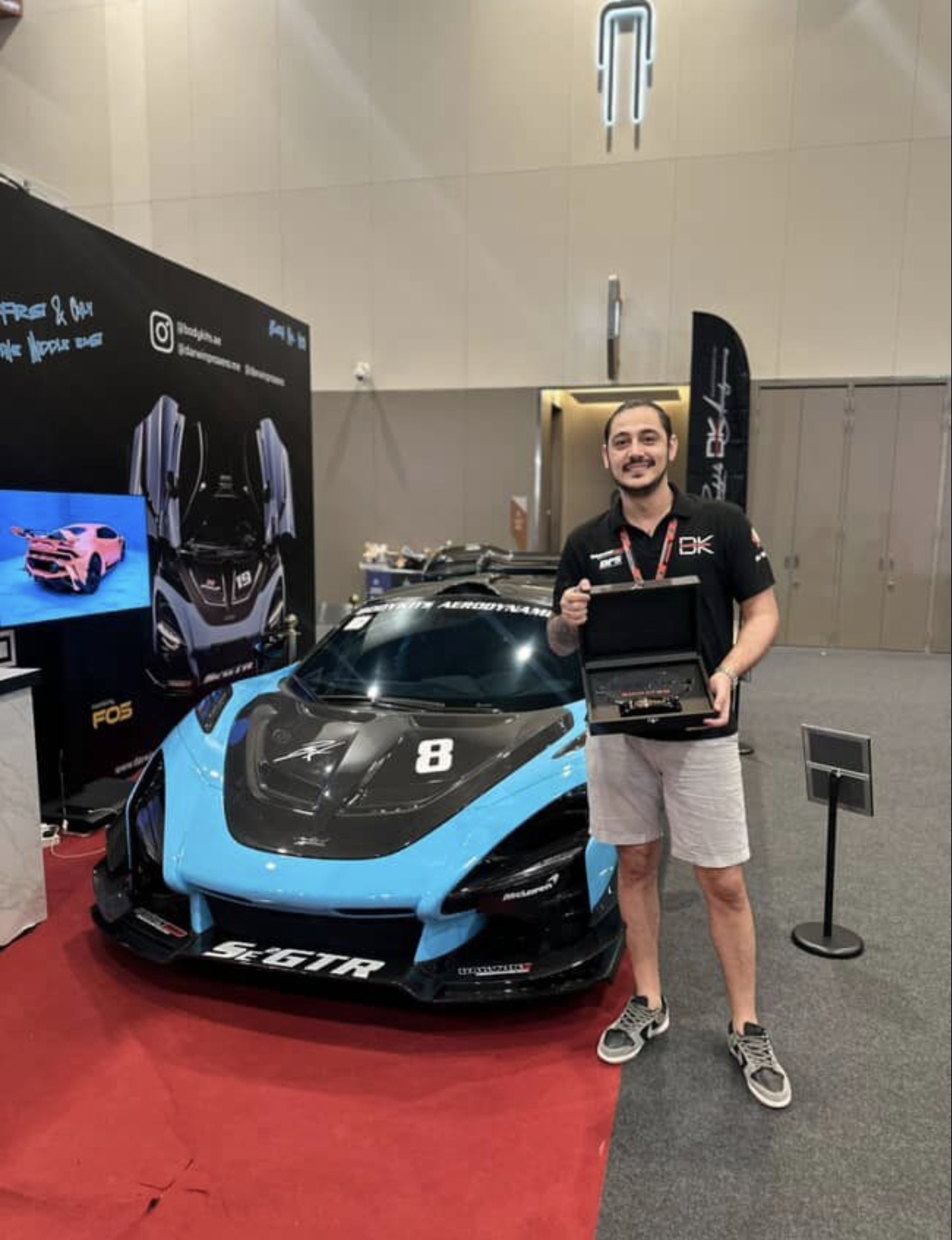 Walid Riachy of Bodykits.ae standing next to the McLaren GTR build at the booth, holding the Best BodyKit Trophy award.
